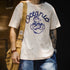 Person wearing a white t-shirt with blue graphic design, holding a beige bag.